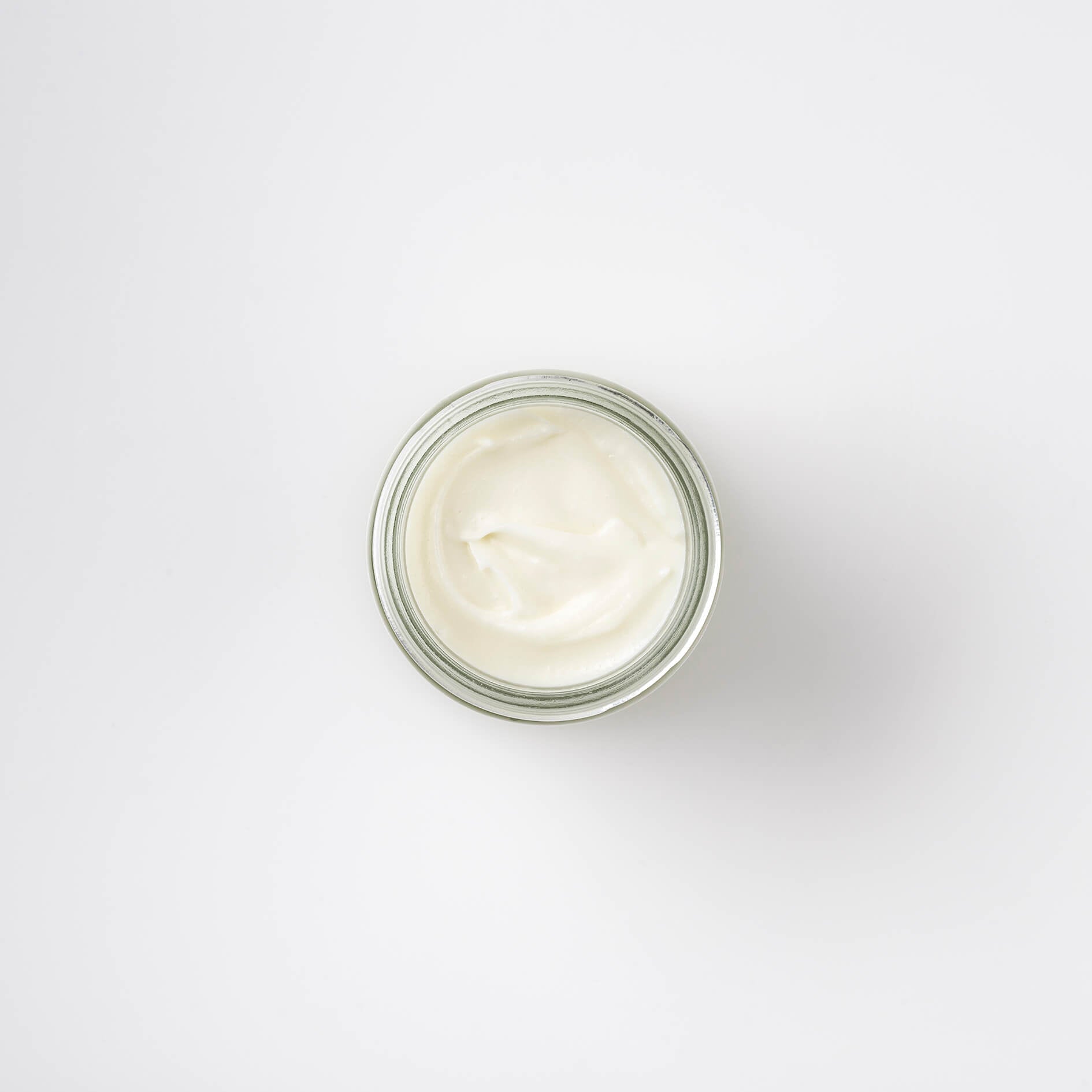 Top view of a 60ml clear glass jar of Bristolmade rose geranium face cream, showing the creams smooth, white surface inside.