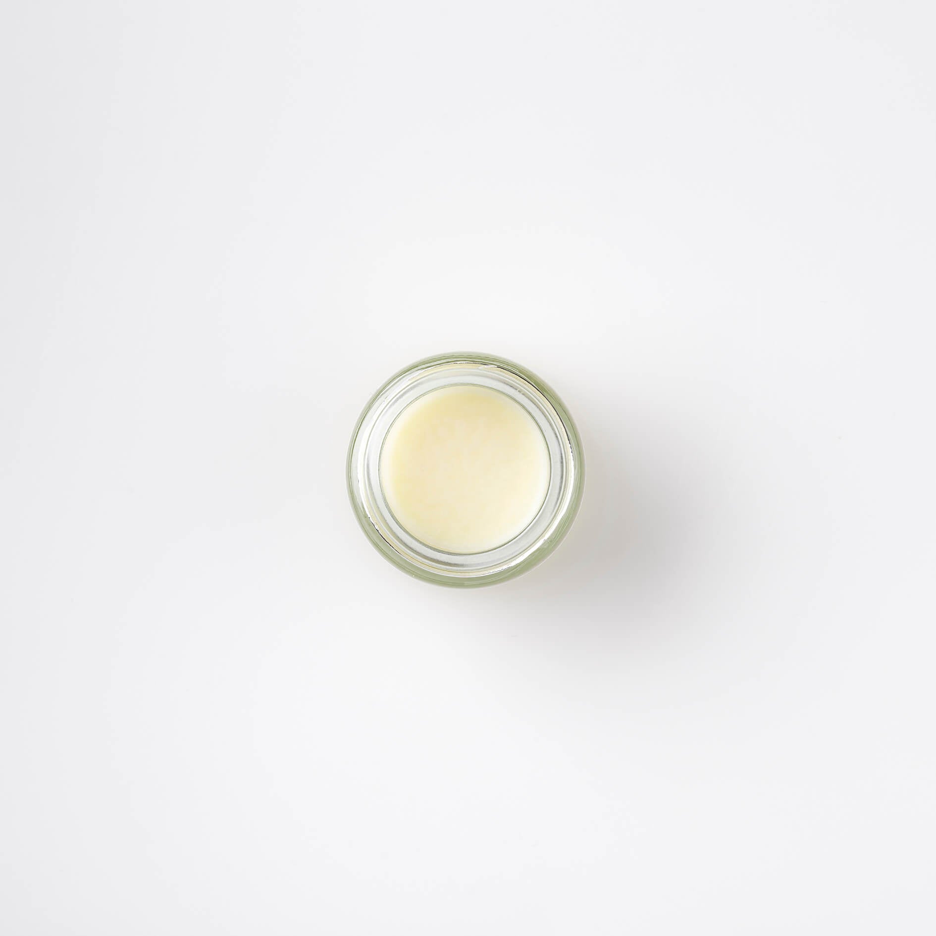 top view of a lime and mint Bristolmade lip balm, in a round, clear glass jar. The product is an off white, glossy colour, showing the smooth properties of the product.