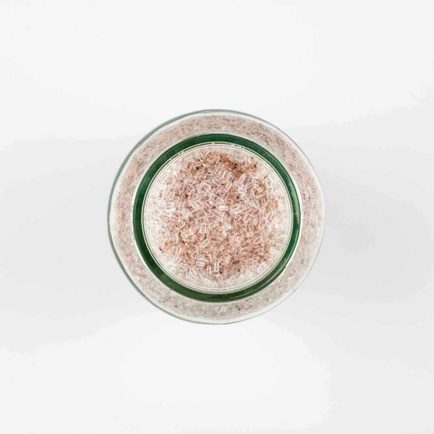 Photo of the top view of a clear glass jar of pale pink bath salts made by The Joy of Meno brand