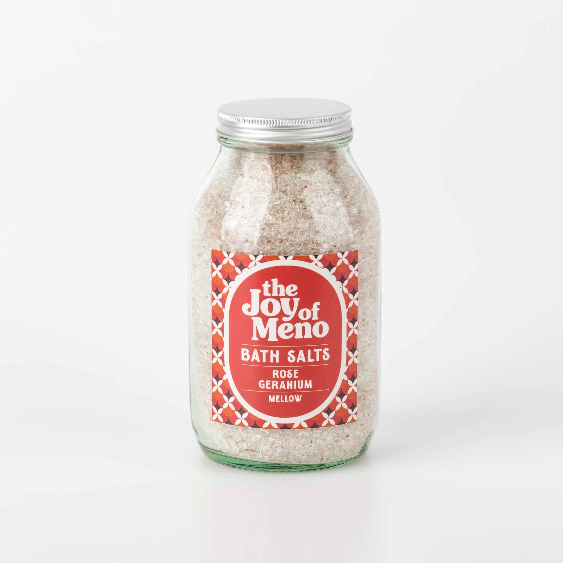 photo of a 500ml clear glass full of pale pink bath salts, with a pink, black and white patterned label with white text showing the brand name, The Joy Of Meno and the product name.